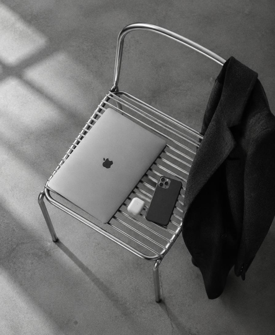 Laptop, phone and earbuds resting on a metal chair beside a black coat
