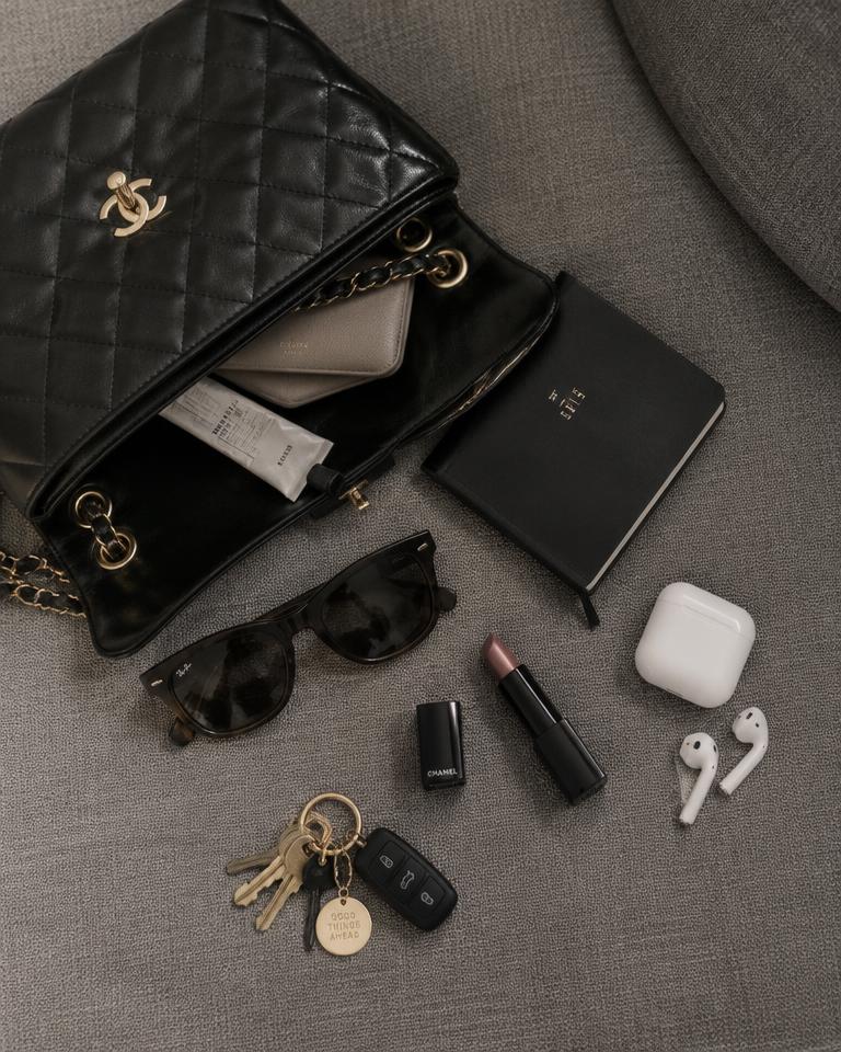 Open black handbag with sunglasses, lipstick and earbuds on a sofa